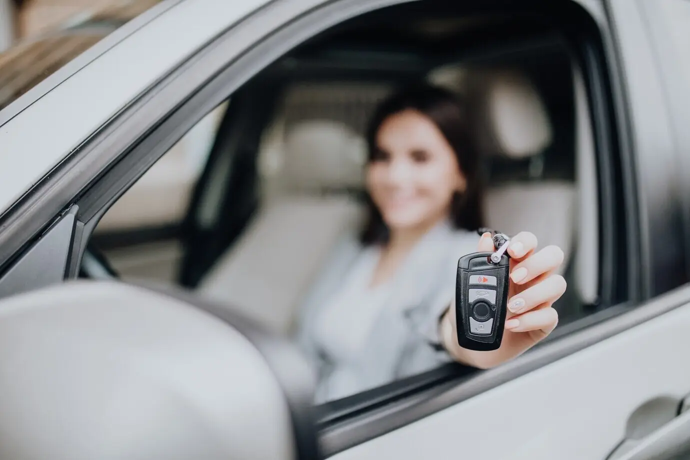 Una mujer joven y feliz junto al coche con las llaves en la mano. Concepto de compra de automóvil. Enfoque en la llave.
